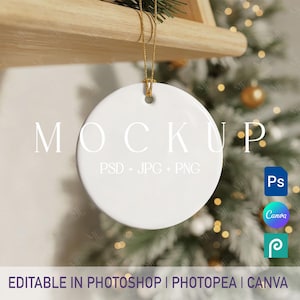 Puede incluir: Un adorno redondo de cerámica blanca con una cuerda dorada, colgado frente a un árbol de Navidad. La palabra "MOCKUP" está impresa en el adorno. El texto "PSD + JPG + PNG" está debajo. Las palabras "EDITABLE IN PHOTOSHOP | PHOTOPEA | CANVA" están en la parte inferior.