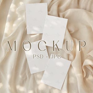 Puede incluir: Cuatro tarjetas rectangulares blancas en blanco dispuestas sobre un fondo de tela beige. La palabra "MOCKUP" se muestra en una fuente serif sobre el texto "PSD + JPG". La tela tiene pliegues y sombras suaves.