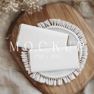 Könnte beinhalten: Zwei weiße Schokoladenriegel-Mockups auf einem Holzbrett mit einer runden weißen Fransenmatte. Der Text "MOCKUP PSD + JPG" ist auf das Brett gedruckt.
