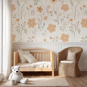 May include: A nursery scene featuring a light wood crib with white bedding, a woven wicker chair, and a large white teddy bear on a beige rug. The wall is adorned with a floral wallpaper in soft peach and beige tones, creating a serene and inviting atmosphere.