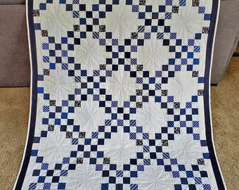 May include: A white quilt with a navy blue and white checkered pattern. The quilt is quilted with a swirling design.