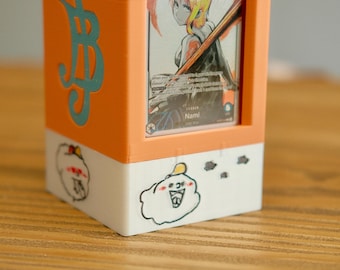 May include: A rectangular card holder with an orange frame and white base. The holder features a card with a character illustration. The orange side has a teal design. The base has cartoon cloud drawings.
