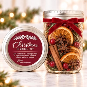 May include: A clear glass mason jar filled with dried orange slices, cinnamon sticks, star anise, cranberries, and rosemary, topped with a red velvet ribbon. The lid features a maroon label reading Christmas SIMMER POT.