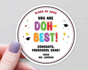 May include: A round sticker with a white background and a red dotted border. The text "CLASS OF 2025" is at the top, with "YOU ARE DOH-BEST!" in colorful letters. "CONGRATS, PRESCHOOL GRAD!" and "FROM MS. LINDSAY" are also included.