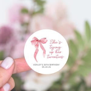 May include: A white round sticker with a pink bow and the text "She's tying up her twenties" and "Ashley's 30th Birthday 05.24.25".