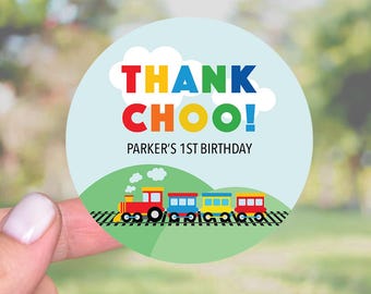 May include: Round thank you sticker featuring a colourful train on a green background. The text reads "Thank Choo! Parker's 1st Birthday."