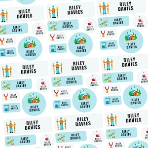 Può includere: Un motivo ripetuto di adesivi azzurri e bianchi con il nome "RILEY DAVIES". Gli adesivi presentano illustrazioni di sciatori, impianti di risalita, baite e medaglie. Gli adesivi sono progettati per l'etichettatura.
