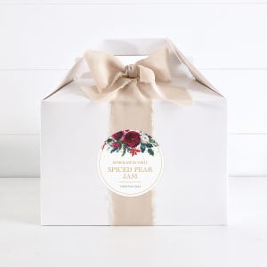May include: A white gift box with a beige ribbon and a round sticker. The sticker has a red and white floral design and gold text that reads "Homemade by Emily Spiced Pear Jam Christmas 2021".