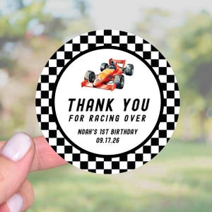 May include: A round sticker with a black and white checkered border. The center features a red and orange race car illustration. Text reads "THANK YOU FOR RACING OVER" and "NOAH'S 1ST BIRTHDAY 09.17.26".