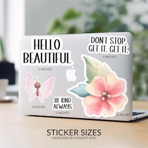 a laptop with stickers on its surface, including a butterfly and a flower. The stickers have motivational messages and sizes.