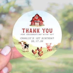 May include: A round sticker with a farm theme. The sticker features a red barn, a cow, a pig, and chickens. The text "THANK YOU" and "FOR CELEBRATING WITH US!" are displayed. The text "CHARLIE'S 1ST BIRTHDAY 08.17.26" is also included.