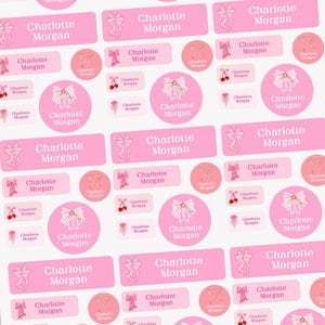 Peut inclure: Étiquettes nominatives roses et blanches personnalisées avec le nom "Charlotte Morgan". Les étiquettes présentent des illustrations de nœuds et de cerises. Étiquettes rectangulaires et circulaires.