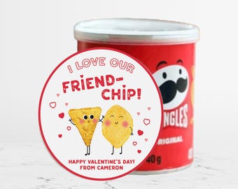 Può includere: Un adesivo rotondo bianco con testo rosso che dice "Adoro il nostro amico-chip!" con un'immagine di cartone animato di due patatine sorridenti. L'adesivo è posizionato su una lattina rossa di patatine con la parola "NGLES" visibile.
