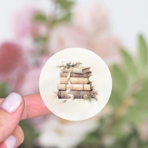 May include: A stack of five vintage books tied with a white ribbon and decorated with a sprig of greenery. The books are brown, beige, and cream with gold accents.