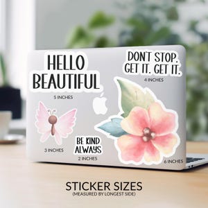 a laptop with various stickers on its surface, including a butterfly and a flower. The stickers have inspirational messages and sizes provided.