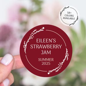 May include: A round, burgundy sticker with white text reading "Eileen's Strawberry Jam Summer 2025." The sticker is encircled by a white floral design. A smaller white circle with "58+ Colors Available" is also visible.
