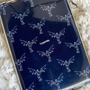 Puede incluir: Una funda de teléfono azul oscuro con un patrón blanco repetido de figuras con alas. El texto "ILLYrian BABY" está impreso en blanco en la funda.