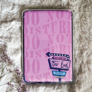 May include: A pink phone case with a white border and a retro motel sign that says "Welcome to The One Bed Inn". The sign has a red border and white lights. The background of the case is covered with the words "Do Not Disturb" repeated in a pink color.