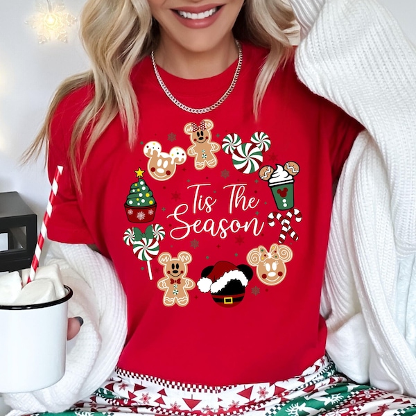 Könnte beinhalten: Ein rotes Kurzarm-T-Shirt mit einer kreisförmigen Grafik aus weihnachtlichen Symbolen wie Lebkuchenmännern, Pfefferminzbonbons, einem Weihnachtsbaum und einer Weihnachtsmütze. Der Schriftzug "Tis The Season" ist in weißer Schreibschrift gedruckt.