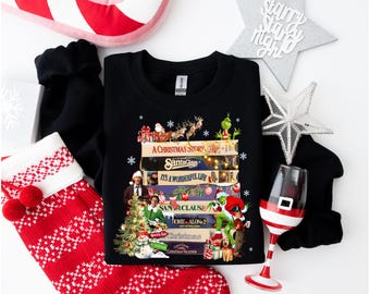 May include: A black crewneck sweatshirt featuring a graphic print of stacked VHS tapes labeled with classic holiday movie titles including A Christmas Story, Santa Claus, It's a Wonderful Life, The Grinch, The Santa Clause, Home Alone 2, and Christmas Vacation.