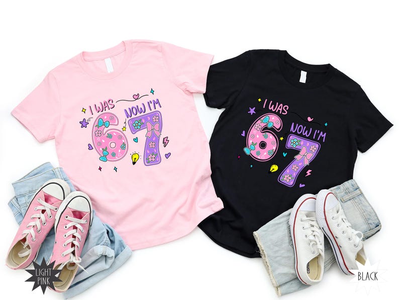 May include: A light pink t-shirt and a black t-shirt, each featuring a graphic with the text 'I WAS 6 NOW I'M 7' in a colorful, playful font. The design includes illustrations of bows, flowers, and stars. Each shirt is paired with blue denim shorts and sneakers.