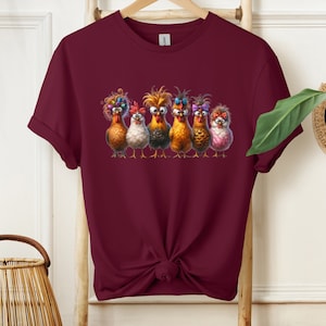 May include: A maroon t-shirt with a graphic of six chickens with colorful feathers and bows. The chickens are looking at the viewer with a funny expression.