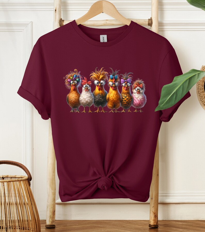 May include: A maroon t-shirt with a graphic of six chickens with colorful feathers and bows. The chickens are looking at the viewer with a funny expression.