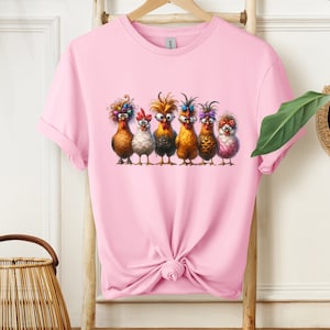 May include: A pink t-shirt with a graphic of six chickens wearing glasses and colorful accessories. The chickens are standing in a row and looking at the viewer.
