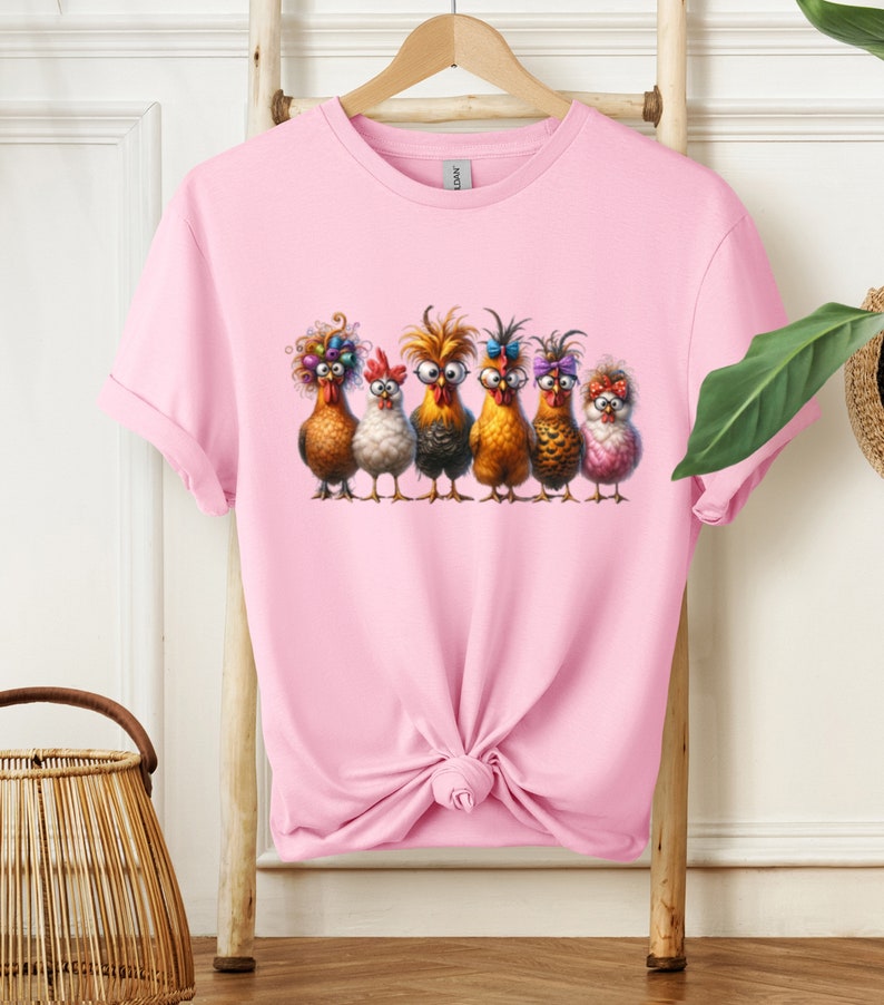 May include: A pink t-shirt with a graphic of six chickens wearing glasses and colorful accessories. The chickens are standing in a row and looking at the viewer.
