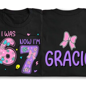 May include: Two black t-shirts featuring colorful graphic designs. The left shirt displays the text I WAS NOW I'M with a pink number 6 and a purple number 7 decorated with flowers and bows. The right shirt features a pink bow and the name GRACIE in purple.