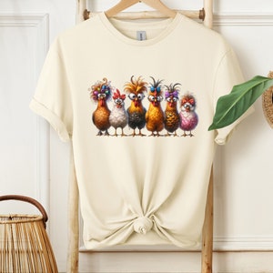May include: A cream-colored t-shirt with a graphic of six chickens wearing colorful accessories. The chickens are standing in a row and have different expressions on their faces.