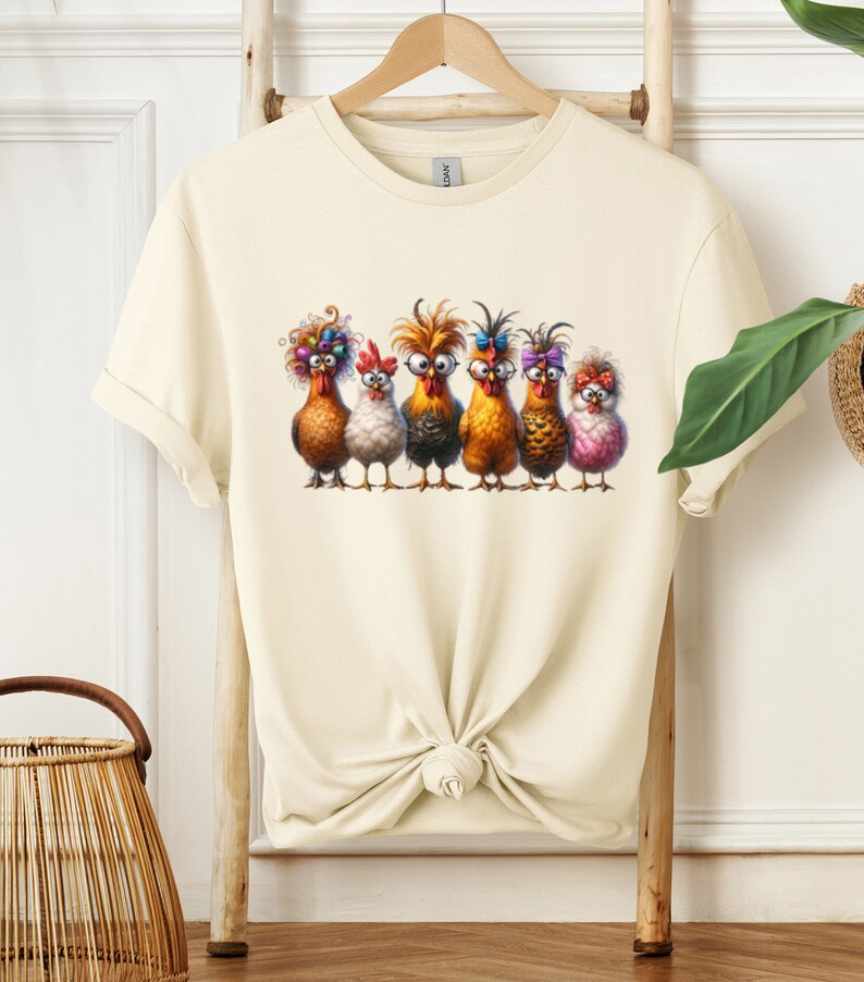 May include: A cream-colored t-shirt with a graphic of six chickens wearing colorful accessories. The chickens are standing in a row and have different expressions on their faces.