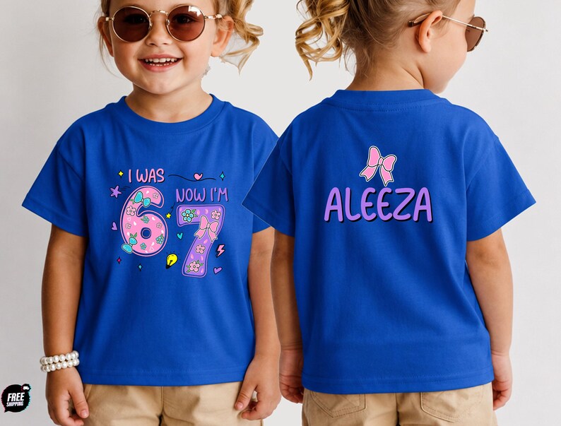 May include: A royal blue t-shirt featuring a front graphic with the text I WAS NOW I'M 6 7 and a back graphic with the name ALEEZA in purple letters. The front design includes pink numbers decorated with small flowers, bows, and colorful icons.