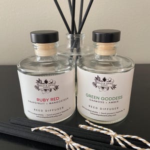 May include: Two glass bottles with black lids and black reed diffusers. The bottles are labeled "Ruby Red Grapefruit + Mangosteen" and "Green Goddess Oakmoss + Amber". Both bottles are labeled "Reed Diffuser" and "100% biodegradable | Hand-poured in Nashville, TN | miloandopalscents.etsy.com".
