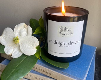 May include: A black candle with a white label that reads "midnight dream" and "NAG CHAMPA". The candle is lit and sitting on a stack of blue books.