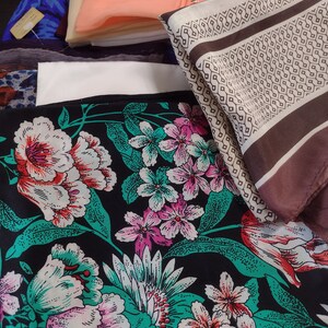 May include: A collection of fabric scraps in various patterns and colors, including floral, geometric, and solid colors. The fabrics are arranged in a pile, with the floral fabric on top.