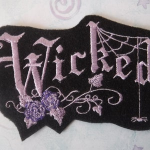 May include: Purple embroidered patch with the word "Wicked" in a gothic font, with a spider web and spider design.