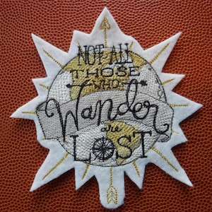 May include: White felt patch with a gold embroidered globe and the text "Not all those who wander are lost".