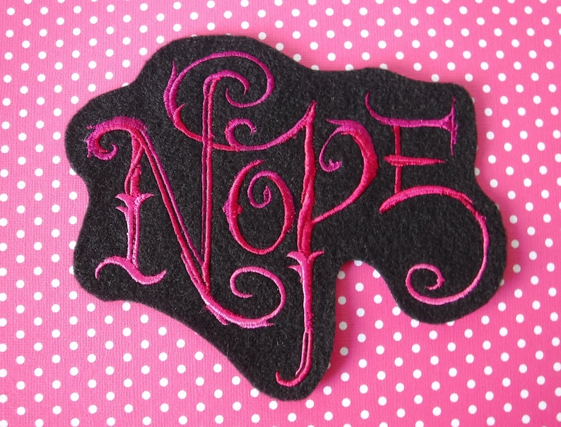 May include: A black felt patch with pink embroidery that reads "Nope" in a stylized font.