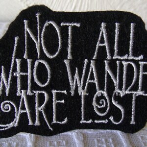 May include: Black fabric patch with white embroidered text that reads "Not all who wander are lost."