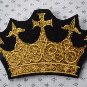 May include: A black felt crown with gold embroidery. The crown has five points and a cross on top.