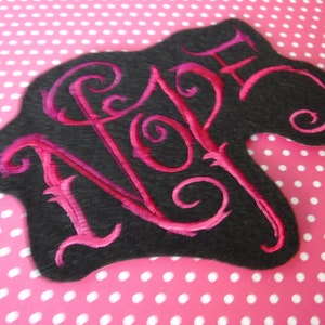 May include: A black felt patch with the word "NOPE" embroidered in pink thread. The letters are in a stylized font with swirls.