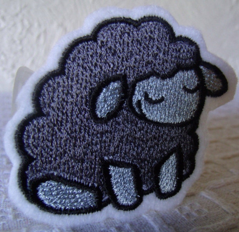 May include: A gray embroidered patch of a sheep with a closed eye expression.