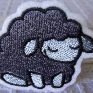May include: A black embroidered sheep with a white face and white legs. The sheep is sitting on a white background.