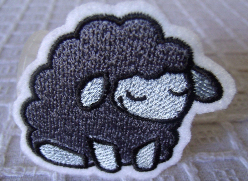 May include: A black embroidered sheep with a white face and white legs. The sheep is sitting on a white background.