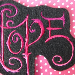 May include: A pink embroidered patch with the word "Hope" in a stylized font on a black felt background.