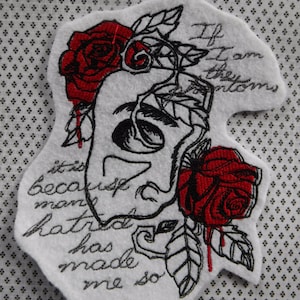 Puede incluir: Parche bordado con un diseño de calavera en blanco y negro, dos rosas rojas y el texto "Si soy un fantasma, es porque el odio del hombre me ha hecho así."
