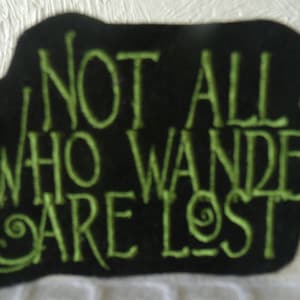May include: Black fabric patch with green embroidered text that reads "Not all who wander are lost".