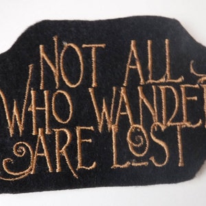 Peut inclure: Patch en feutre noir avec broderie dorée qui dit "Not all who wander are lost."