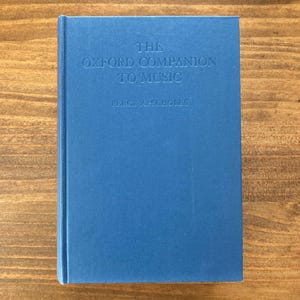 May include: A blue hardcover book titled The Oxford Companion to Music by Percy A. Scholes. The front cover features the title and author name embossed in a matching blue tone, centered on the solid blue surface of the book's front cover.